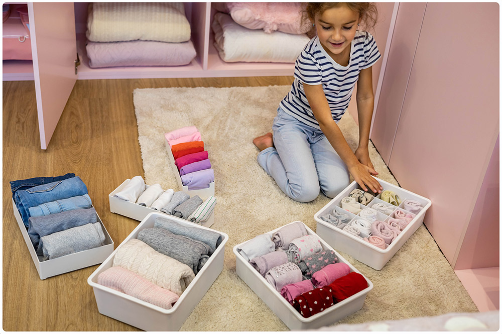 Girl helping to order her clothes inside small boxes by sets: panties, socks, T-shirts, pants, sweater and socks.