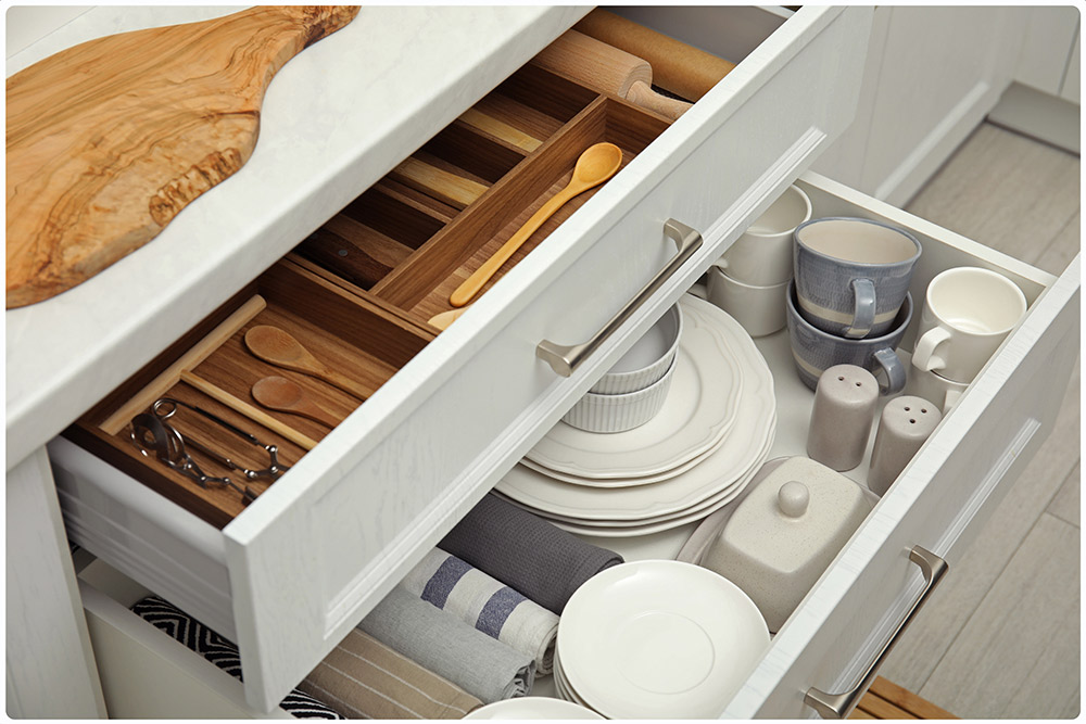 The image shows the interior of kitchen drawers, where kitchen utensils are stored. In the first drawer you can see the wooden cutlery. In the second drawer all the utensils necessary to put the table: cups, plates, tablecloths, salt shakers, sugar bowl, napkin holders, etc.